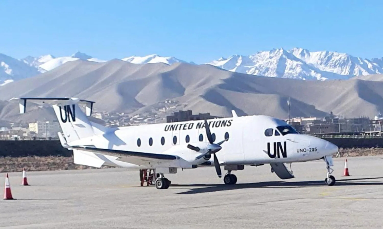 A Beechcraft 1900D in United Nations markings on an apron below snow-capped mountains.