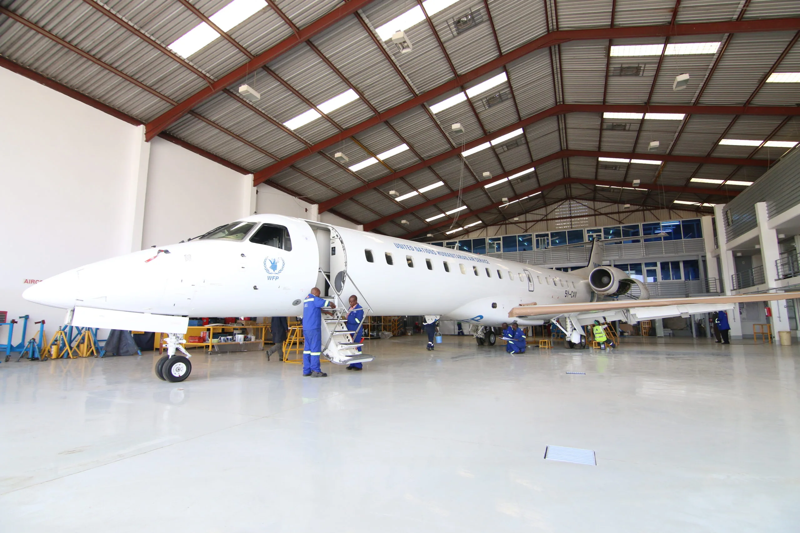 An Embraer ERJ-145 in the ALS hangar, with engineers in blue overalls working around it.