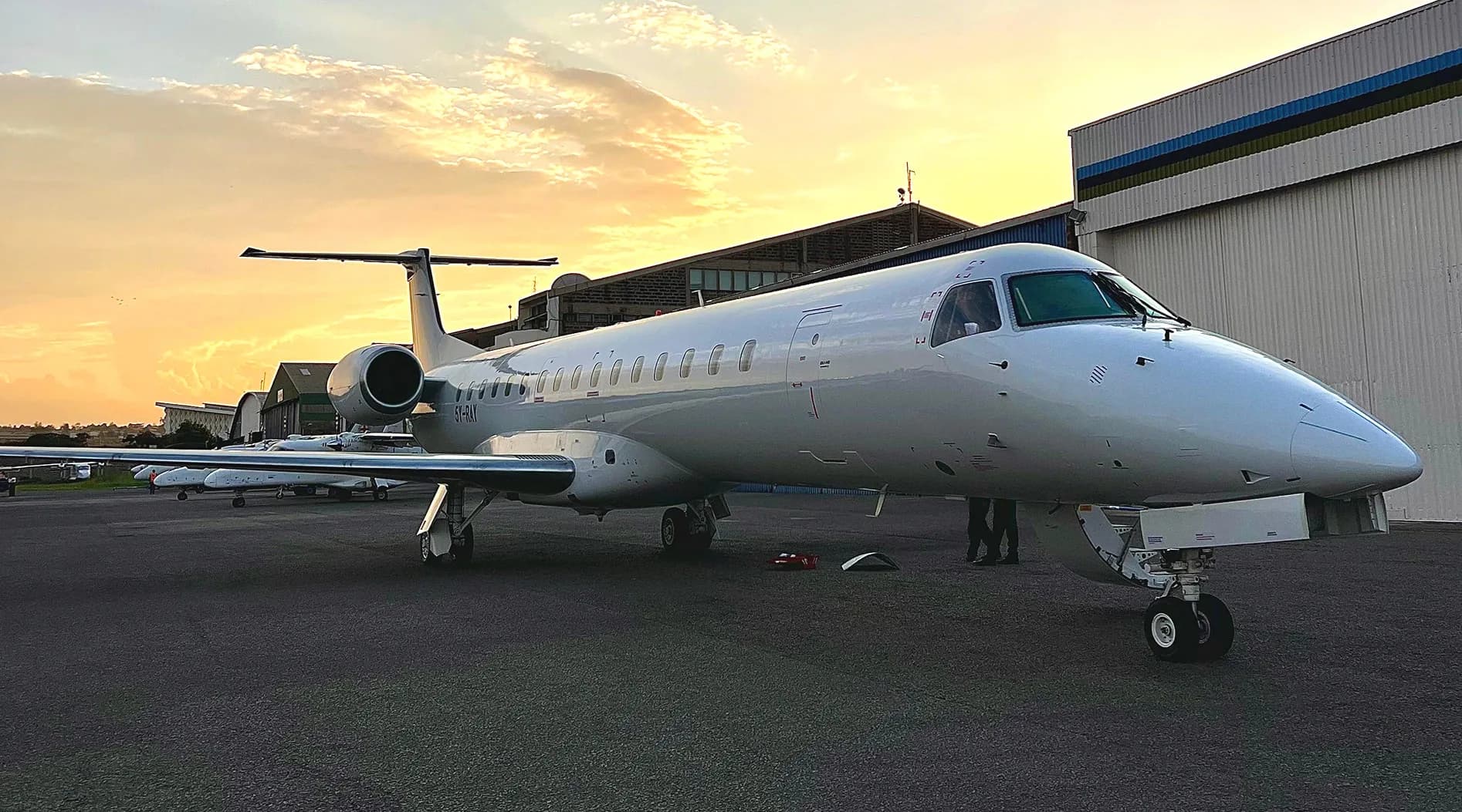 An ALS Embraer ERJ-145 parked outside the hangar under a golden sky.