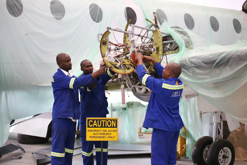 Three ALS engineers in blue overalls working on an aircraft on jacks
