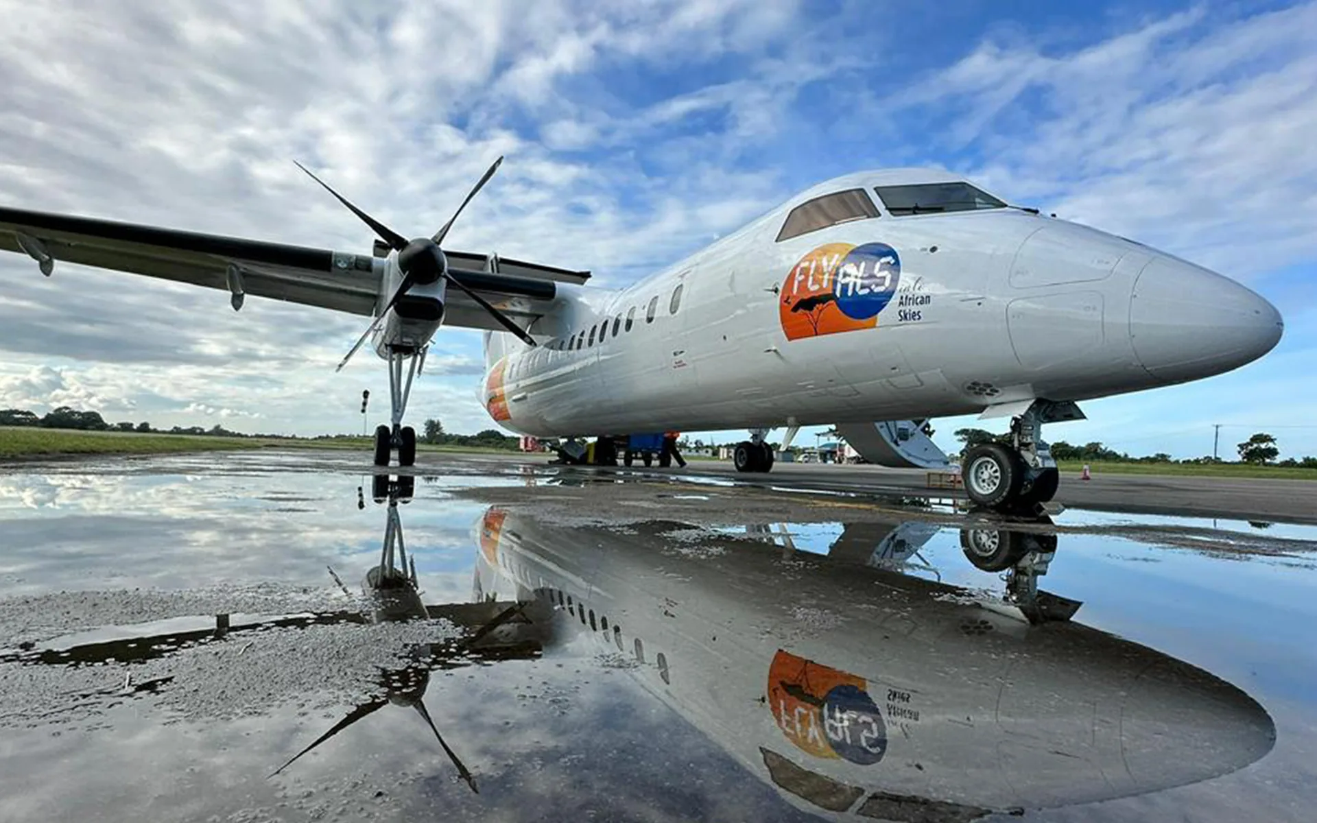 A Dash 8 in Fly ALS colours, reflected in a rain puddle on the apron