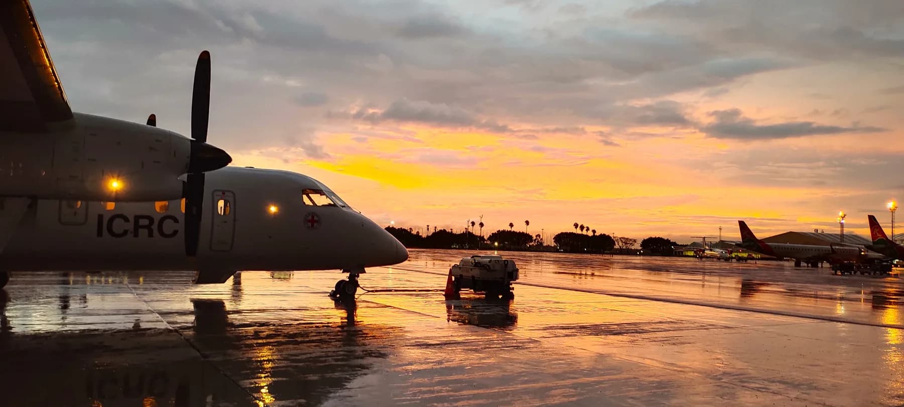 A Dash 8 in Red Cross colours on a wet apron under an orange sky