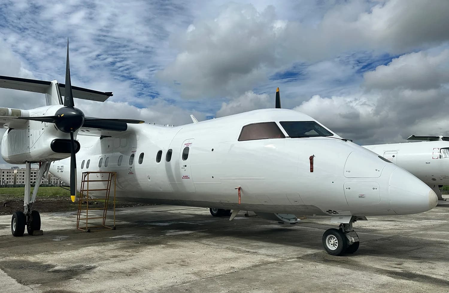 A white Dash 8 on the apron with a maintenance stand at the door
